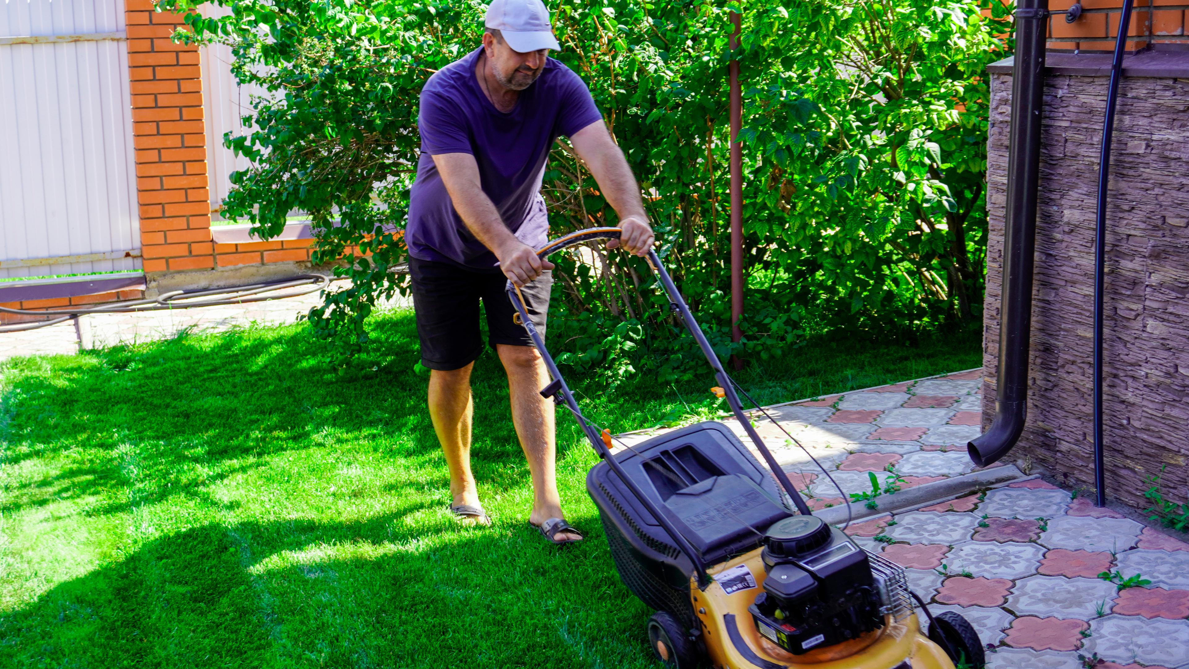 Ein Mann mäht den Rasen seines gartens mit einem Rasenmäher.