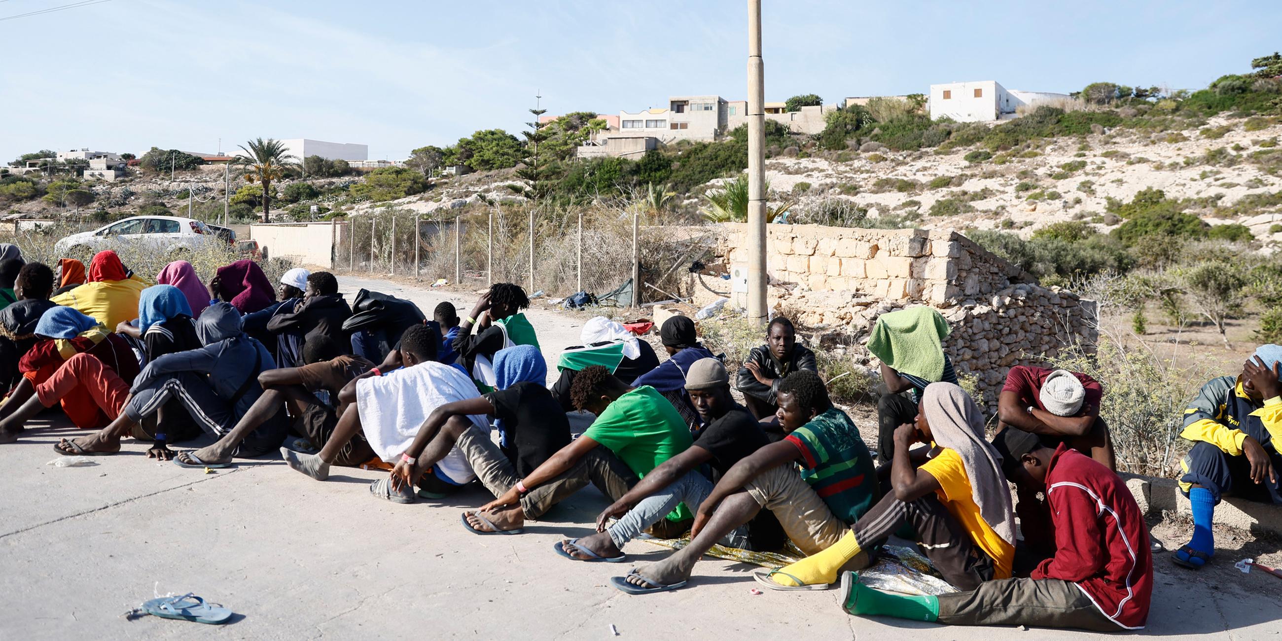 Menschen sitzen vor einem Aufnahmezentrum für Migranten auf der Insel Lampedusa am 15.09.2023.