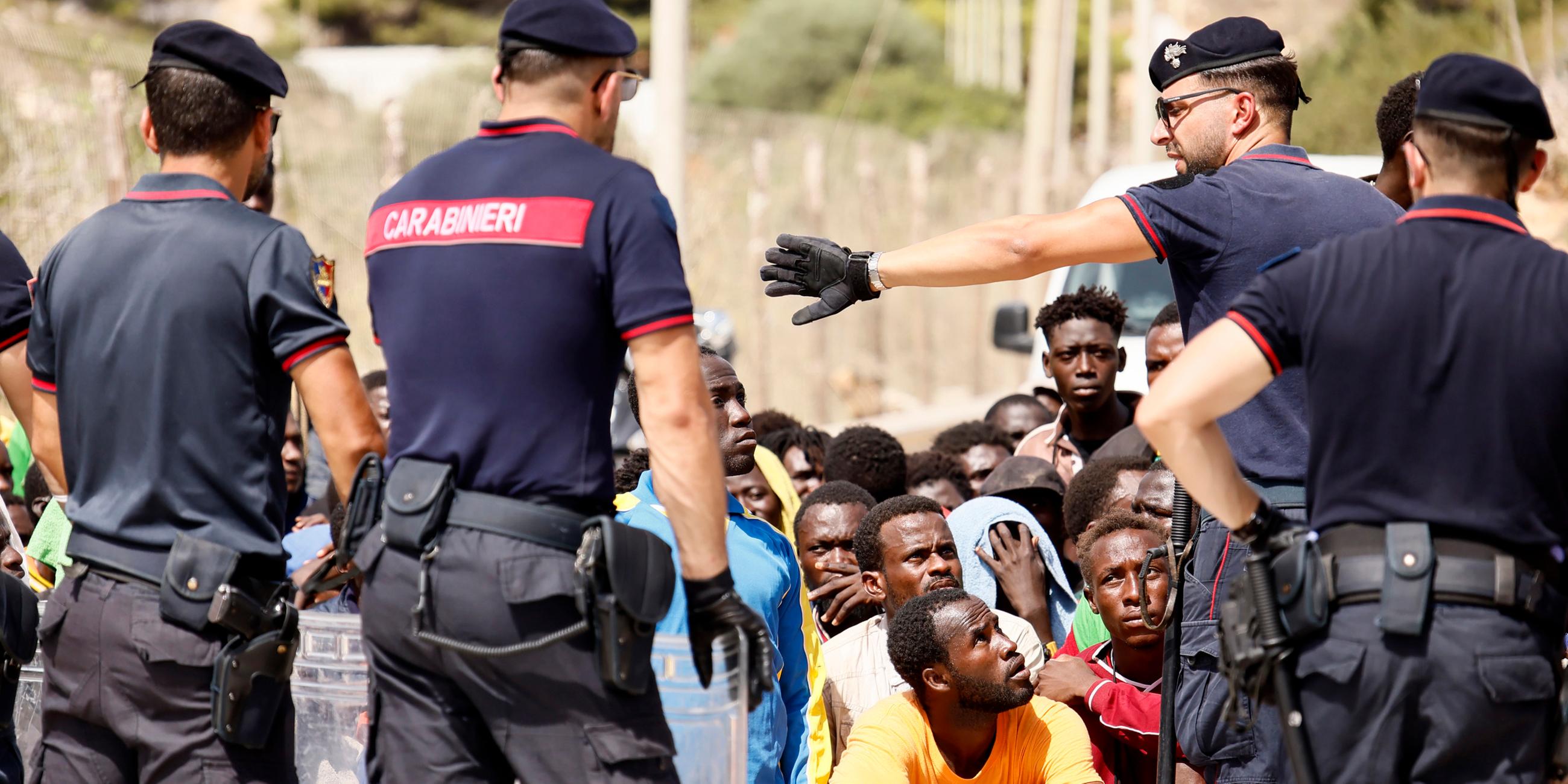 Italienische Polizisten stehen vor einer Gruppe Geflüchteter