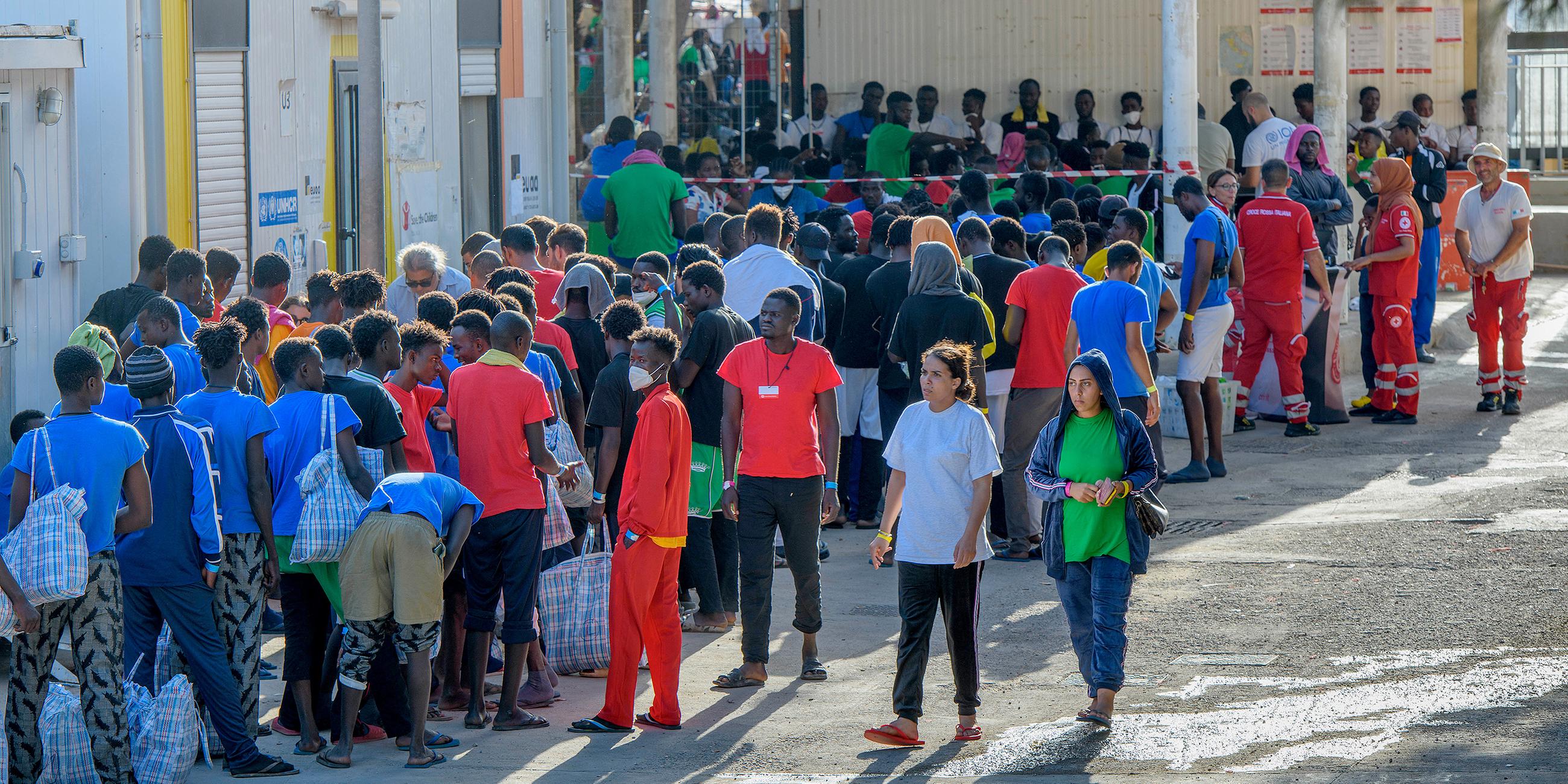 Migranten stehen vor Gebäuden auf der Insel Lampedusa