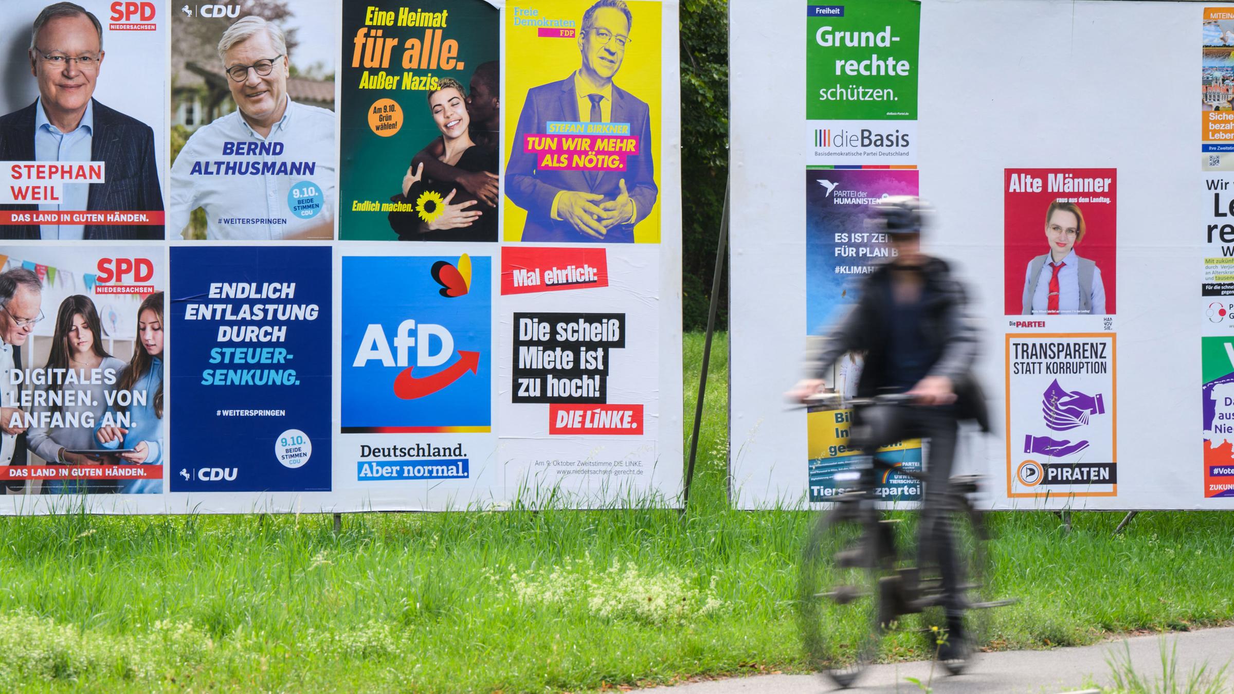 Ein Radfahrer radelt an einer Wand mit Wahlplakaten verschiedener Parteien vorbei. 