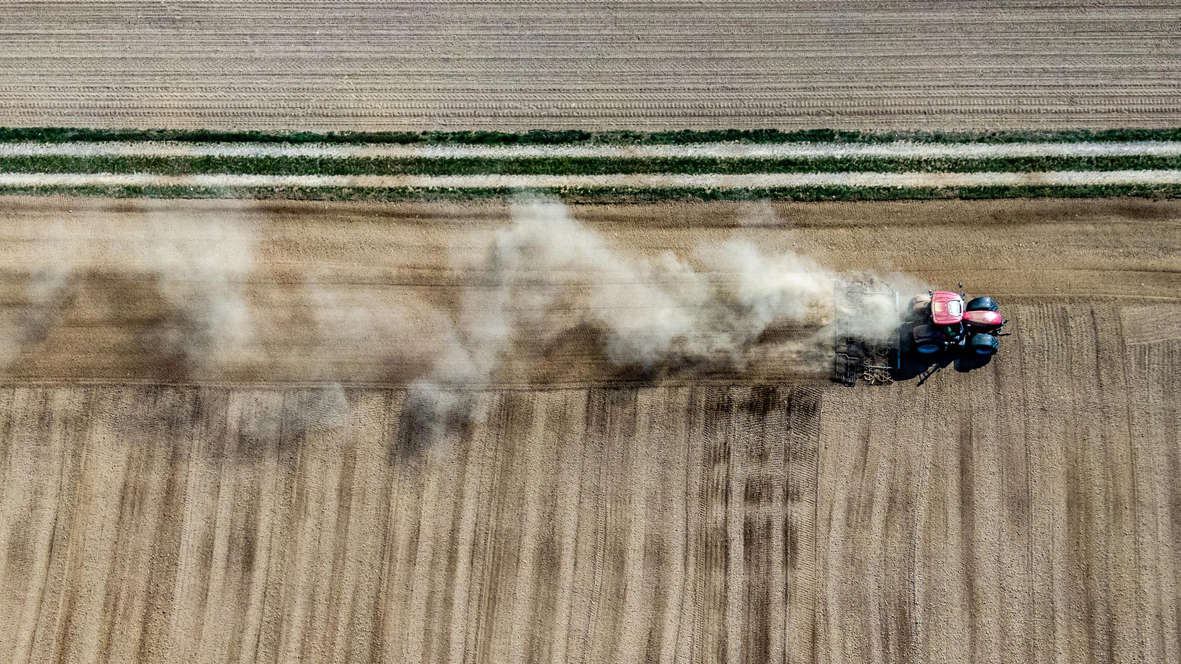 Ein Landwirt wirbelt mit seinem Traktor beim Bearbeiten eines Feldes Staub auf. 