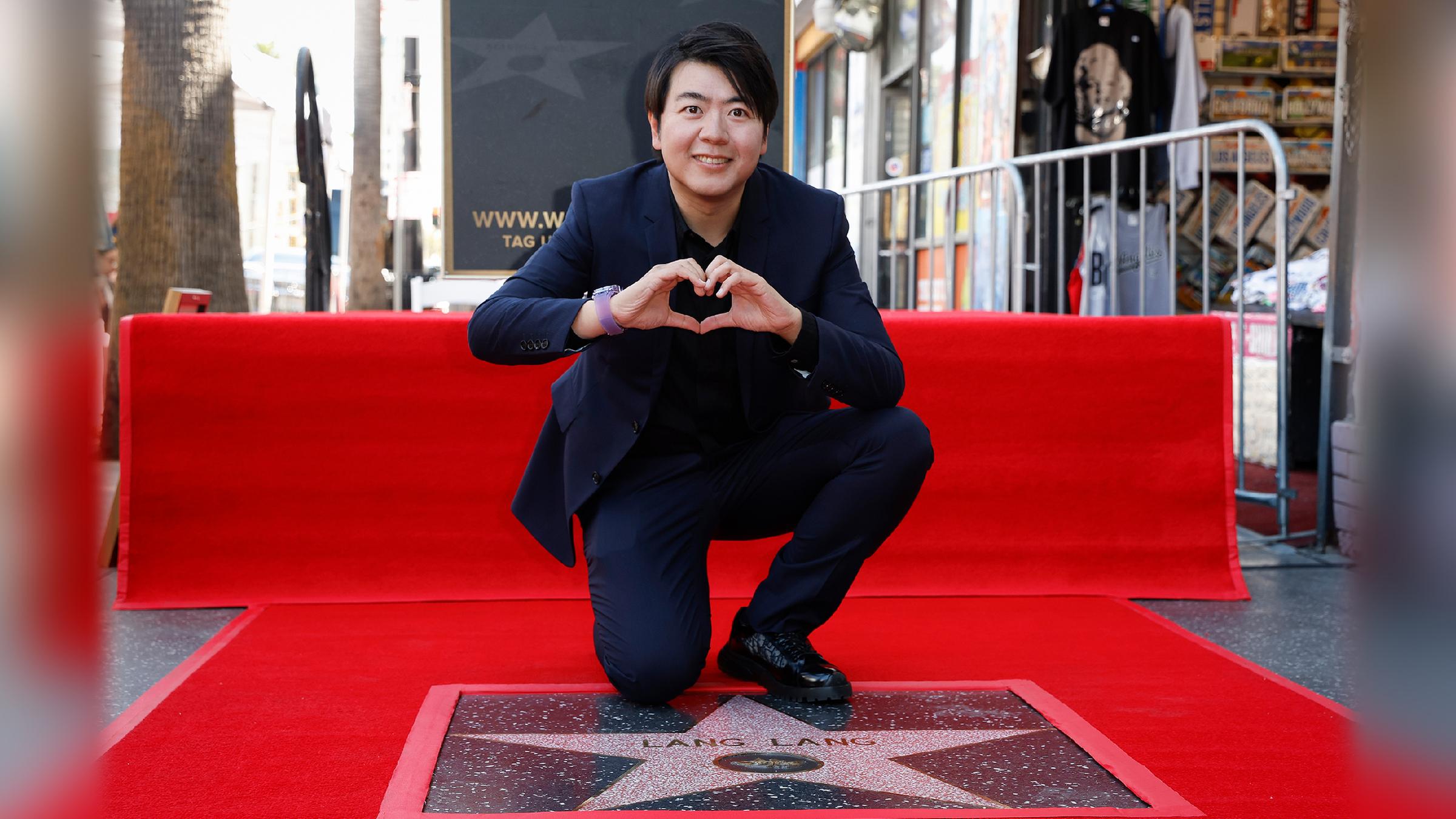 Lang Lang kniet auf dem roten Teppich hinter seinem Stern auf dem Walk of Fame und formt ein Herz mit seinen Händen.