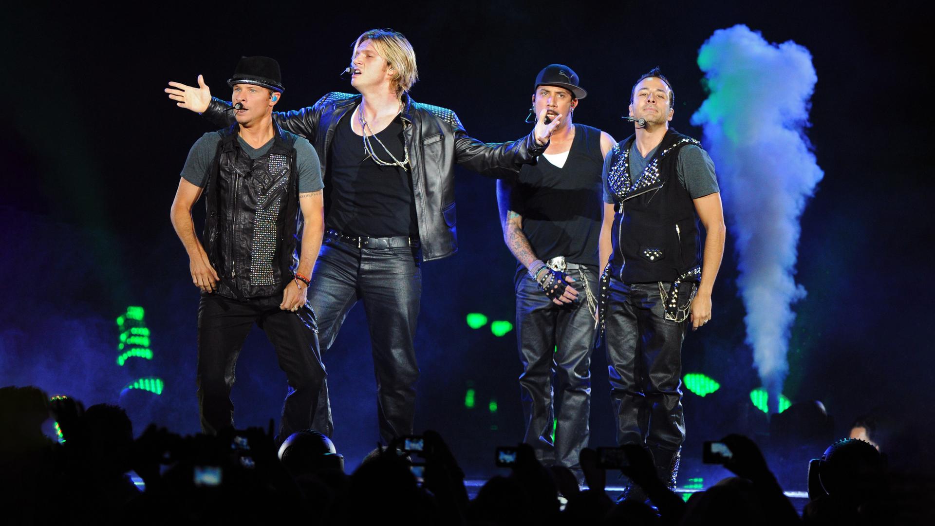 Howie Dorough, Nick Carter, Alexander James McLean und Brian Littrell (l-r), Mitglieder der US-amerikanischen Band Backstreet Boys stehen singend auf der Bühne. Sie sind alle schwarz gekleidet und tragen Lederhosen.