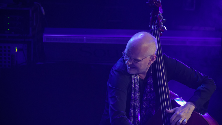 Der Bassist und Cellist Lars Danielsson auf der Bühne der JazzBaltica im blauem Licht, über seinen Bass gebeugt und zur Seite blickenden.