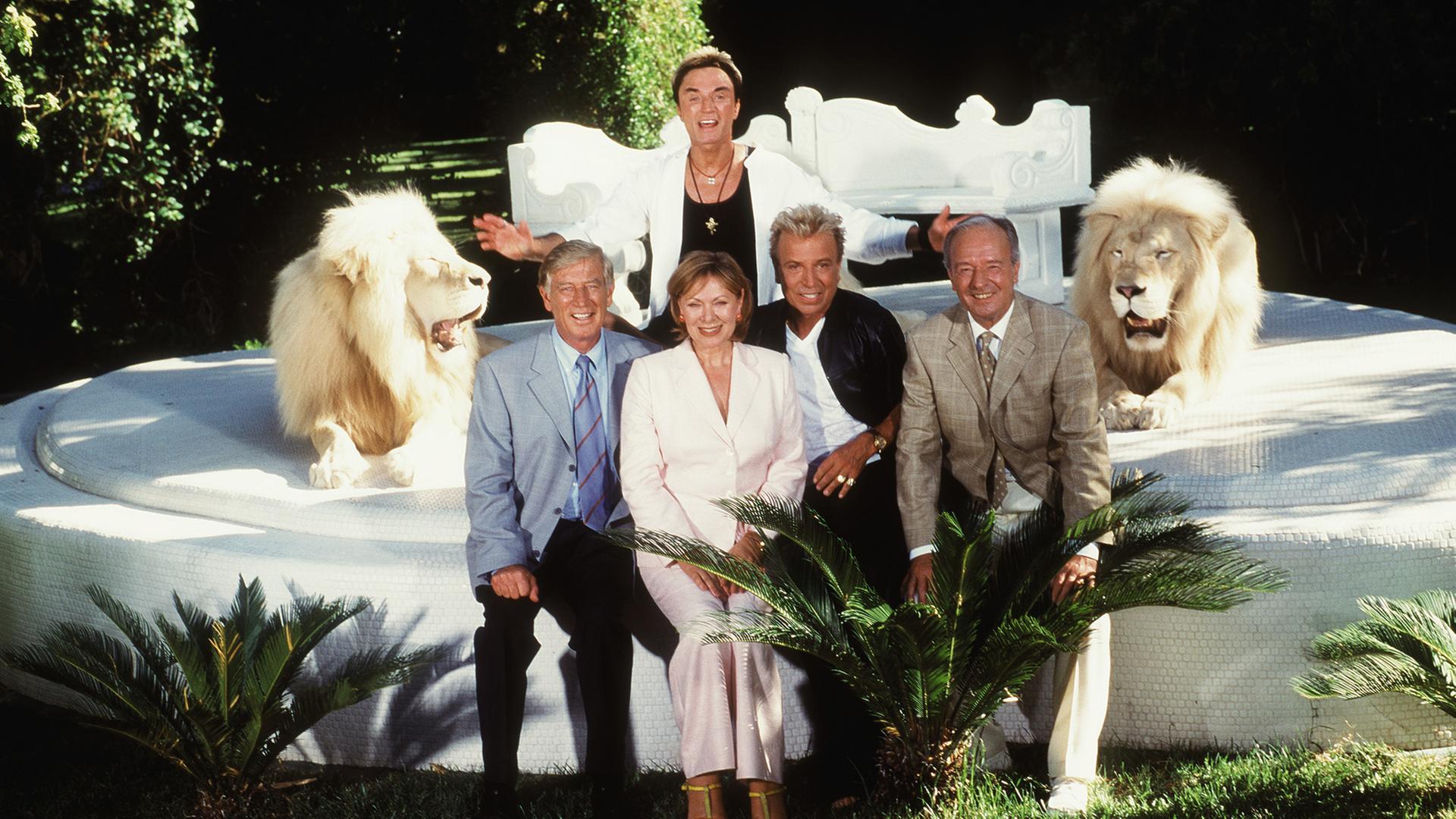 "Das Traumschiff - Las Vegas": Kapitän Paulsen (Siegfried Rauch), Horst Schröder (Horst Naumann) und Beatrice (Heide Keller) sitzen mit Siegfried (Siegfried Fischbacher) und Roy (Roy Horn) eingerahmt von zwei Löwen auf einer Steinplattform.