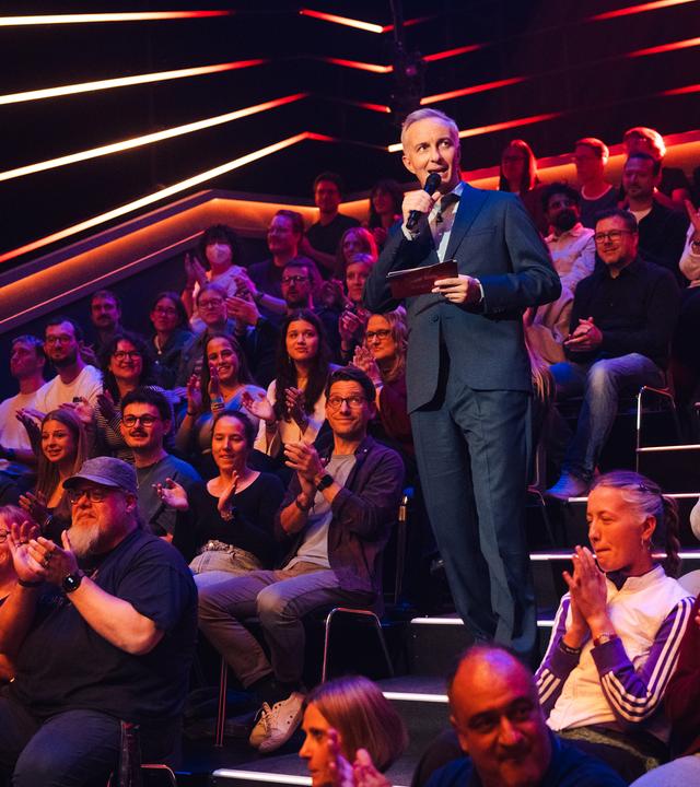 Jan Böhmermann steht auf der Studiotreppe. Links und rechts von ihm sitzt das Studiopublikum.