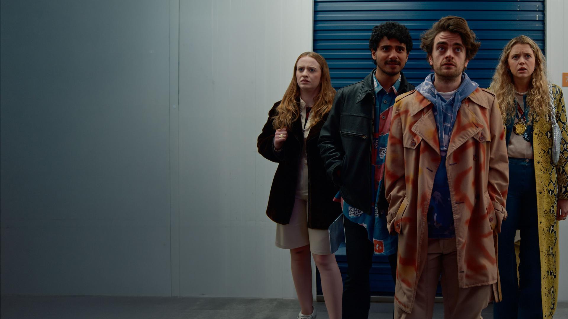 "Extraordinary - Lassen wir's krachen?": Die vier Freunde Jen (Máiréad Tyers), Kash (Bilal Hasna), Jizz (Luke Rollason) und Carry (Sofia Oxenham) stehen alle nebeneinander und schauen nach vorne. Jen wirkt irritiert, hält schwer an ihrer Hängetasche fest. Kash hat die Hände in der Jacke und Jizz schaut verzweifelt in den Lagerraum. Carry wirkt genervt.