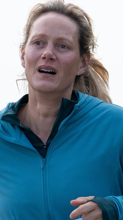 Juliane (Anna Schudt) joggt in einer blauen Laufjacke, mit einer vierstelligen Startnummer auf dem Bauch, auf einer Straße entlang.