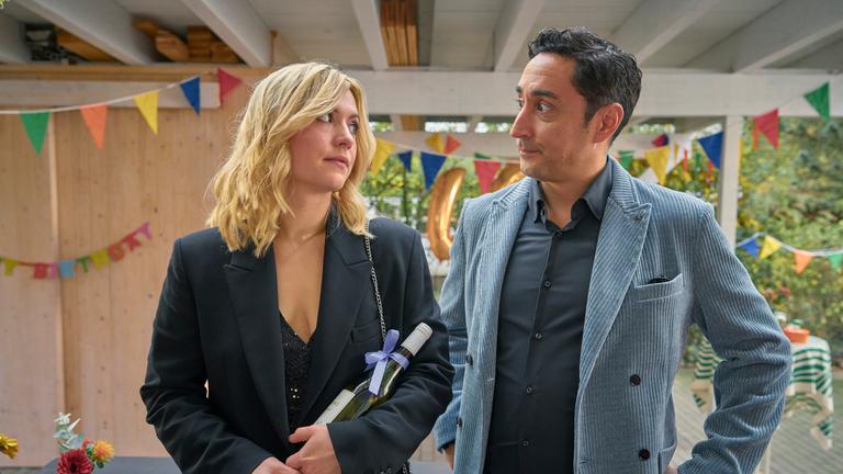 Die Kinderschwindlerin: Nina (Laura Storz) und Sammy (Ekrem Bora, aka Eko Fresh) schauen sich genervt und abwartend an, während sie auf der Veranda von Ninas Schwester stehen, die zu ihrem Geburtstag eingeladen hat