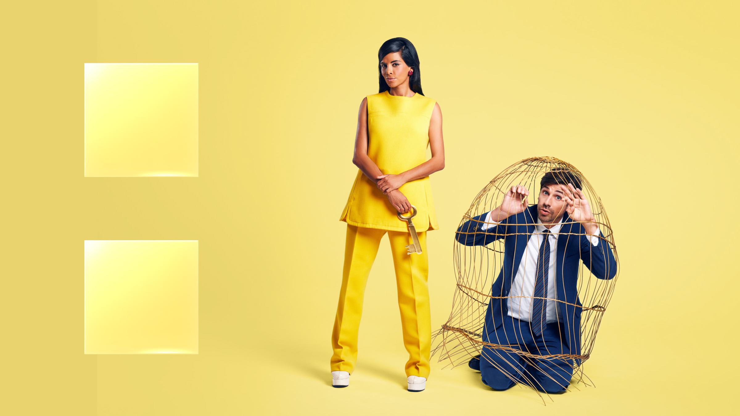 Symbolbild, das Collien Ulmen-Fernandes im gelben Outfit zeigt. An ihrer Seite ein kniender Mann im Anzug, eingepfercht in einem Bambuskäfig.