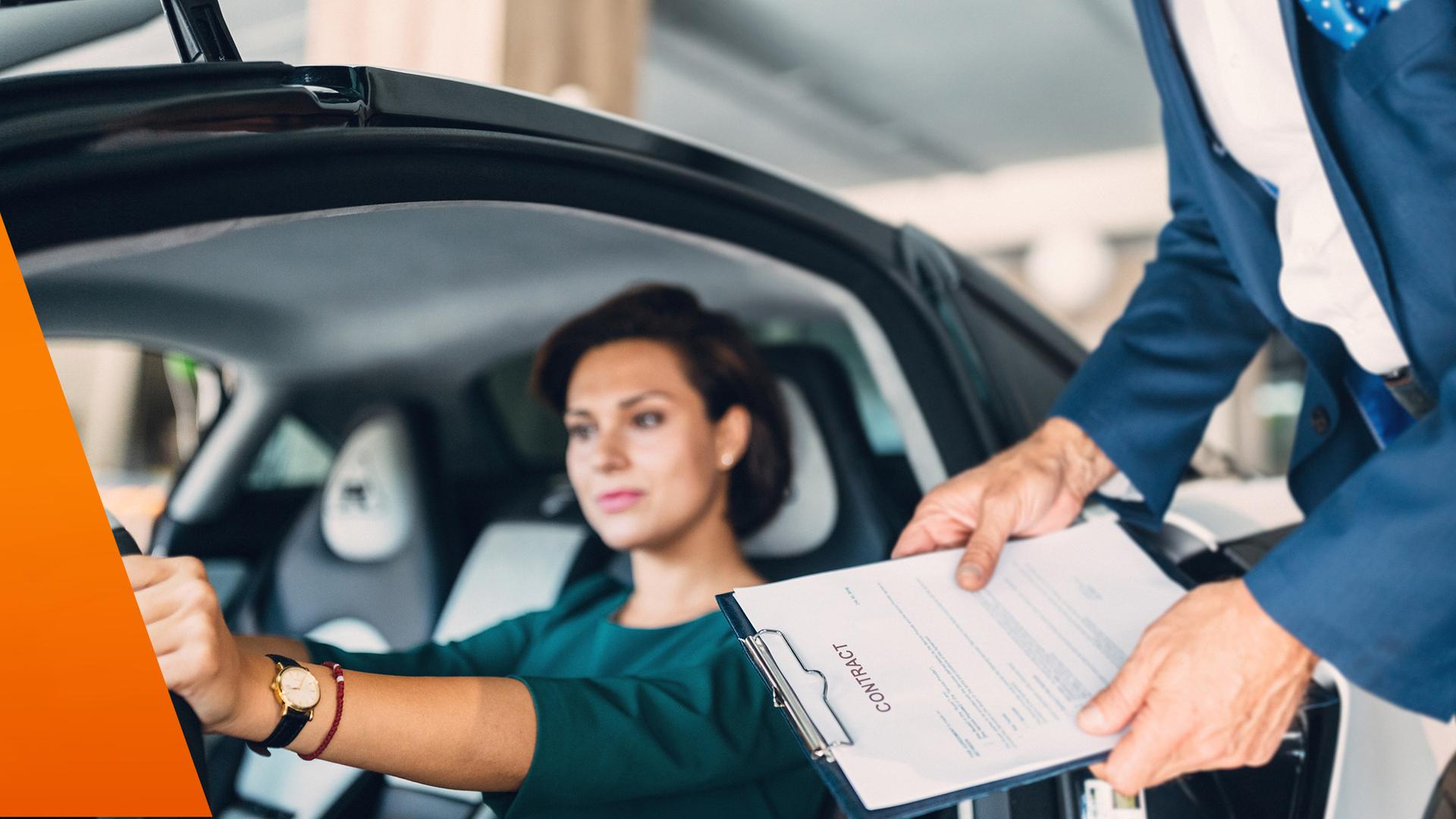 Frau sitzt im Auto, im Hintergrund ein Verkäufer