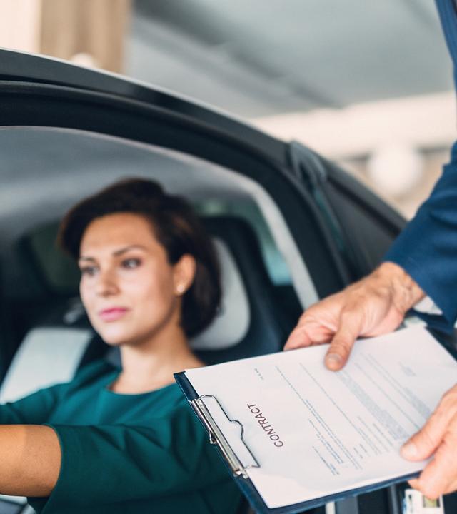 Frau sitzt im Auto, im Hintergrund ein Verkäufer