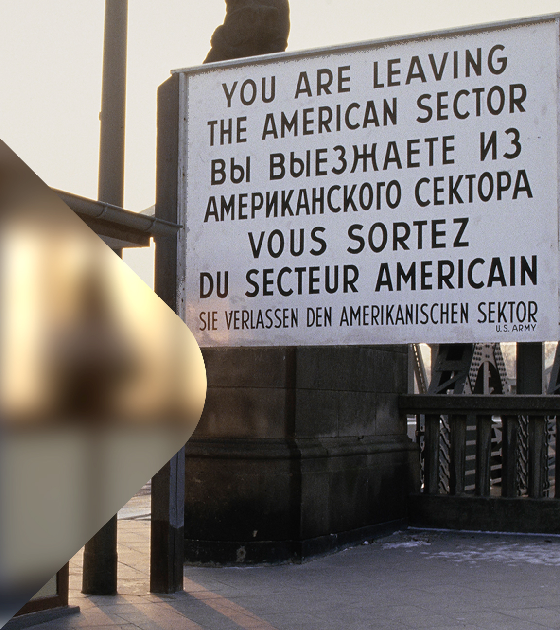 Zu sehen ist ein Grenzübergang mit Wachhaus und einem Hinweisschild zum verlassen des amerikanischen Sektors. 