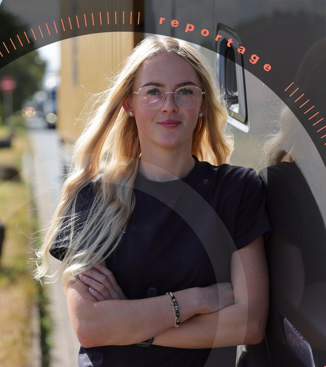 Melina steht neben ihrem Lkw, im Hintergrund befindet sich die volle Autobahn. Sie schaut freundlich in die Kamera.