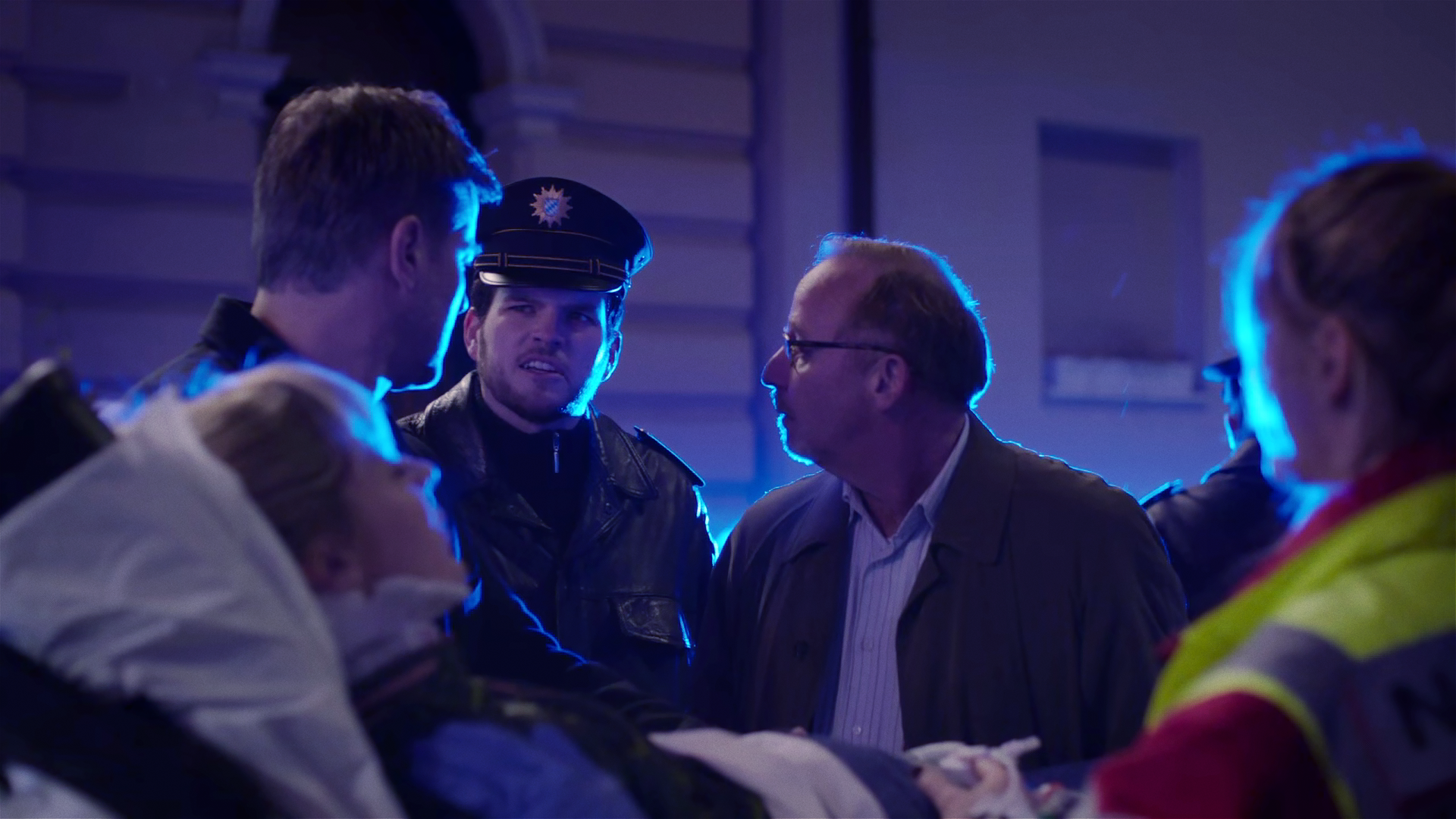 Während eine Frau von Rettungssanitätern auf einer Liege weggerollt wird, spricht Ludwig Schaller (Alexander Held) mit Harald Neuhauser (Marcus Mittermeier) und einem weiteren Polizisten.
