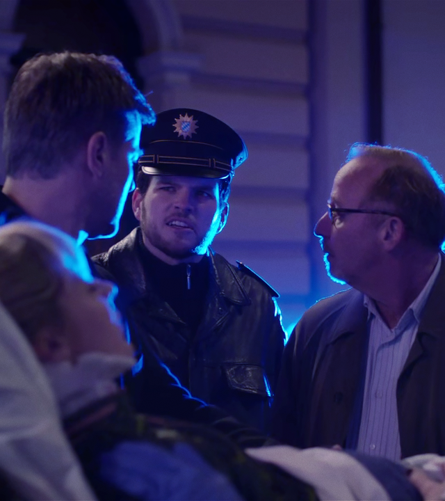 Während eine Frau von Rettungssanitätern auf einer Liege weggerollt wird, spricht Ludwig Schaller (Alexander Held) mit Harald Neuhauser (Marcus Mittermeier) und einem weiteren Polizisten.