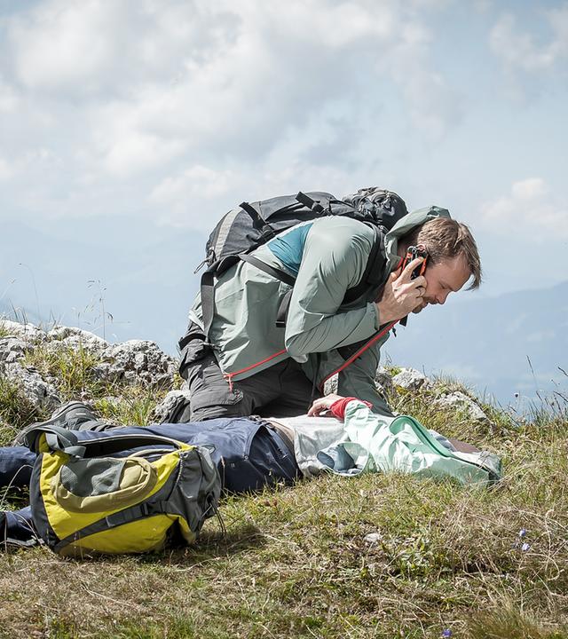 "Der Bergdoktor - Lebendig begraben (1)": Auf der Kuppe eines Berges beugt sich Peter Geis (Matthias Ziesing) über seine auf dem Gras liegende Frau Henriette (Christina Athenstädt).