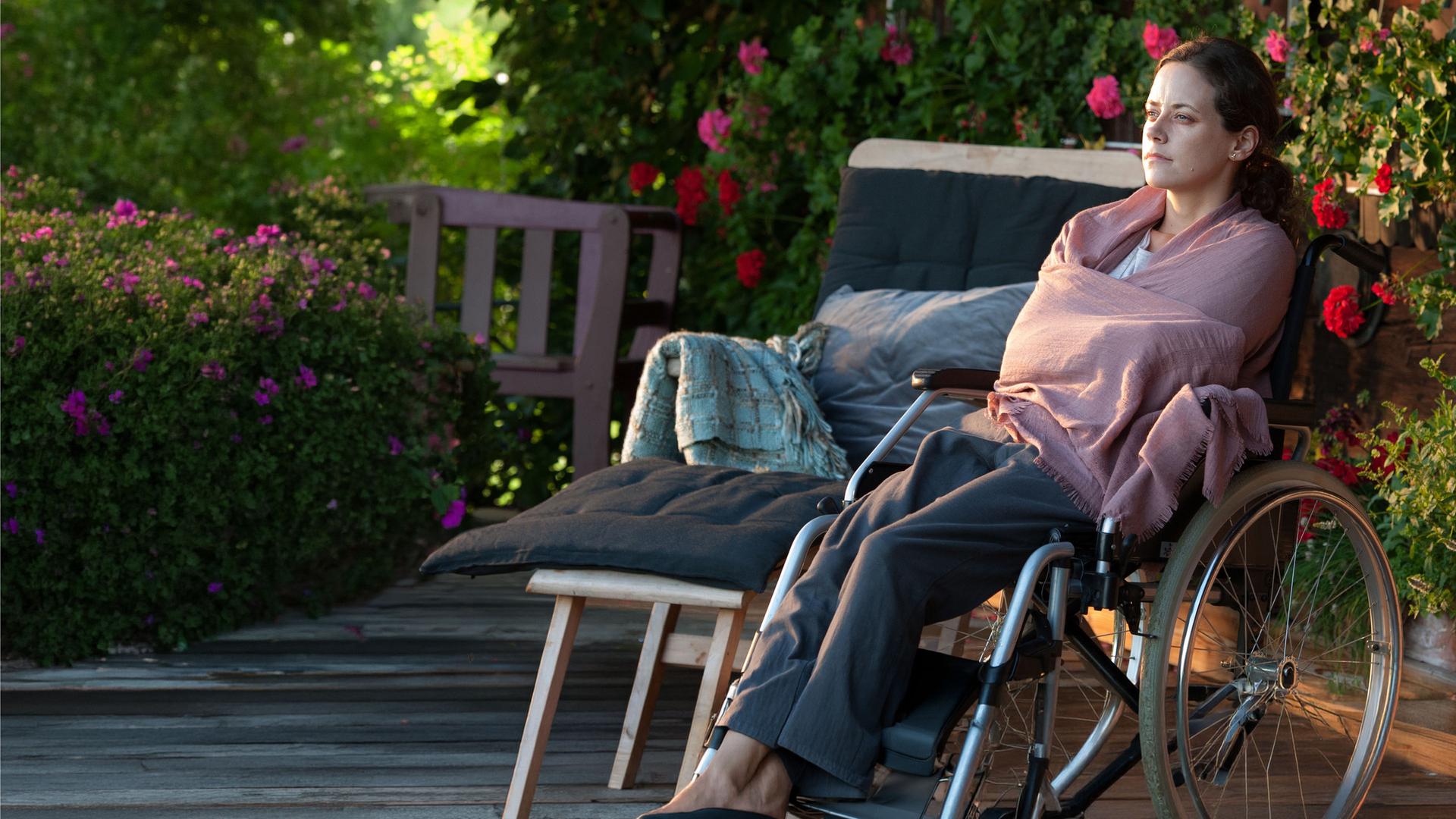 "Der Bergdoktor: Lebensangst (1)": Sandra Lennart (Anja Knauer) sitzt im Rollstuhl vor dem Haus und schaut nachdenklich vor sich hin.