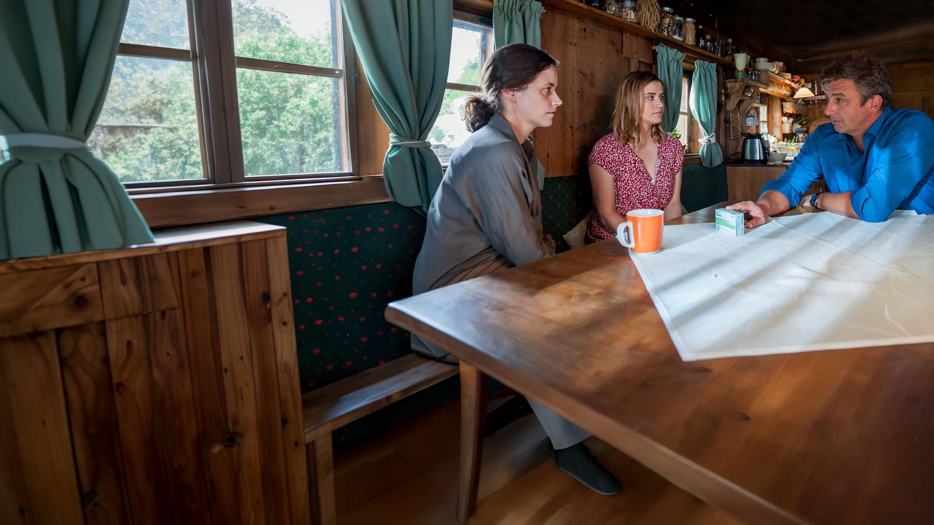 "Der Bergdoktor: Lebensangst (2)": Am Küchentisch sitzen Dr. Martin Gruber (Hans Sigl), Sandra Lennart (Anja Knauer) und Christina Lennart (Morgane Ferru) zusammen und unterhalten sich.