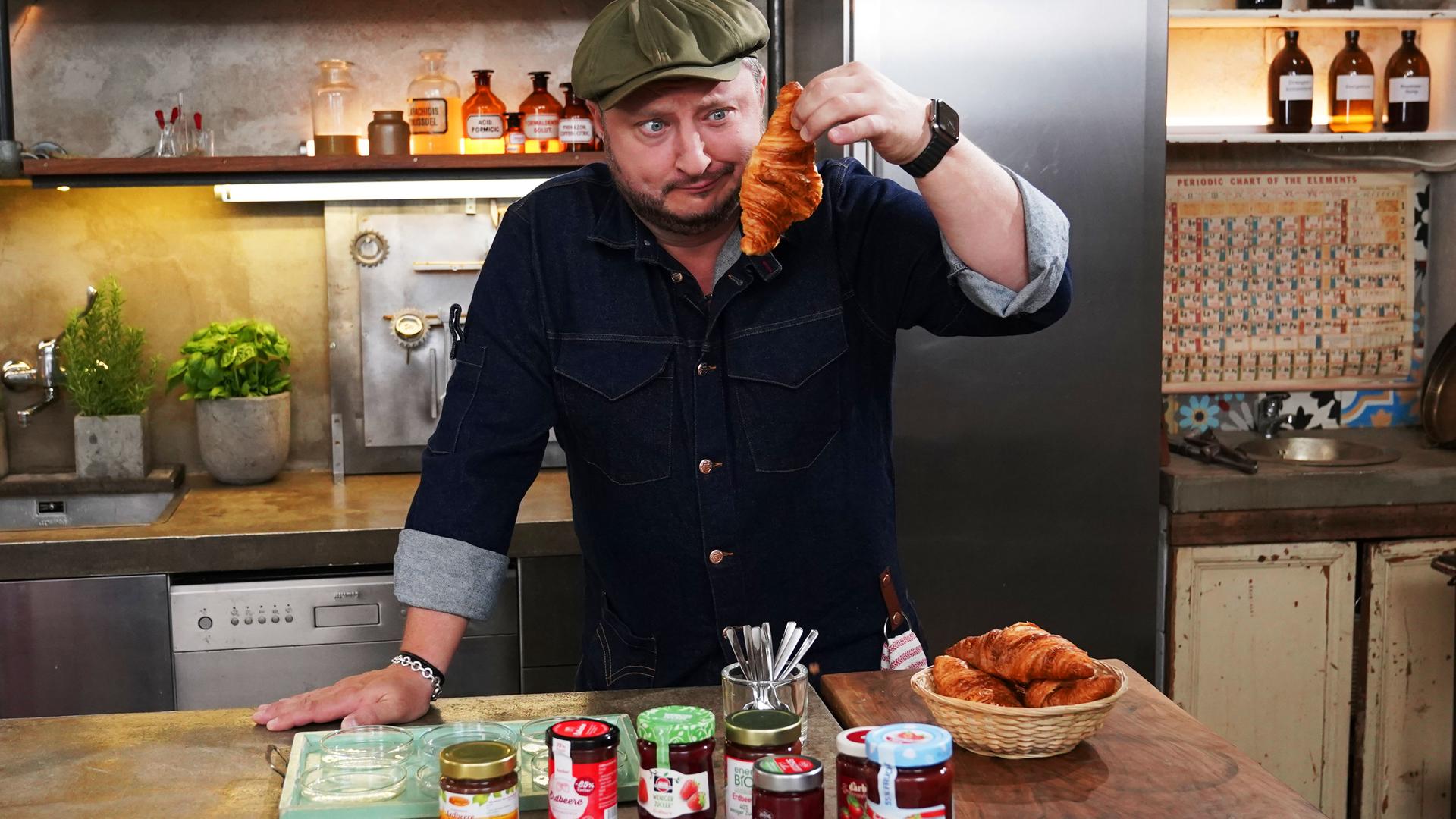 Sebastian Lege hat zuckerreduzierten Fruchtaufstrich eingekauft und wirft einen kritischen Blick auf ein Croissant.
