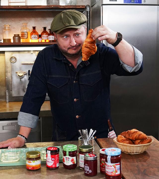 Sebastian Lege hat zuckerreduzierten Fruchtaufstrich eingekauft und wirft einen kritischen Blick auf ein Croissant.