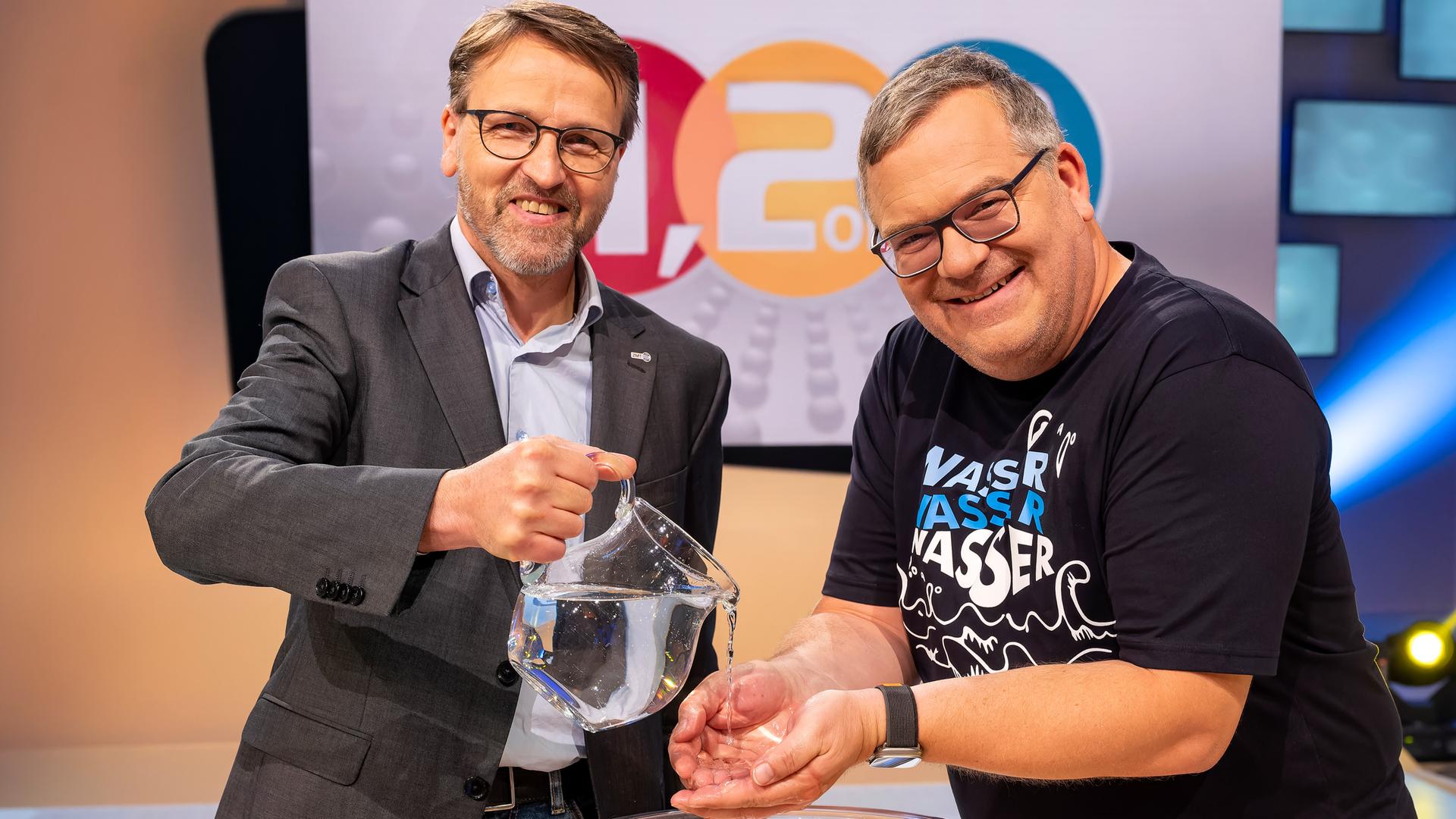 Ökologe Dr. Martin Zimmer steht mit Elton an einem hüfthohen Tisch. Martin Zimmer lässt Elton aus einer Karaffe Wasser über die Hände laufen. Auf dem Tisch steht eine große Schüssel, in dem das Wasser aufgefangen wird.