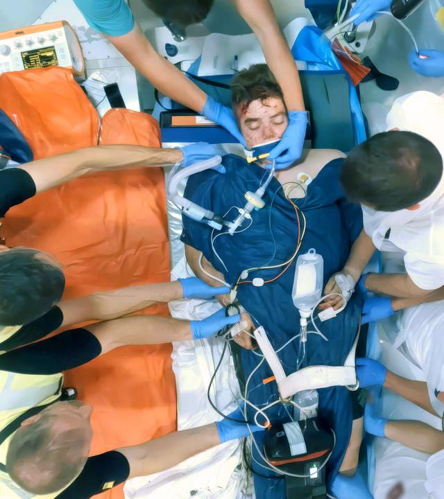 Ein junger Mann wird von mehreren Personen auf eine Krankenliege gehoben.