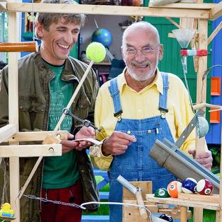 Fritz Fuchs und Peter Lustig stehen an einer Erfindung und lachen.