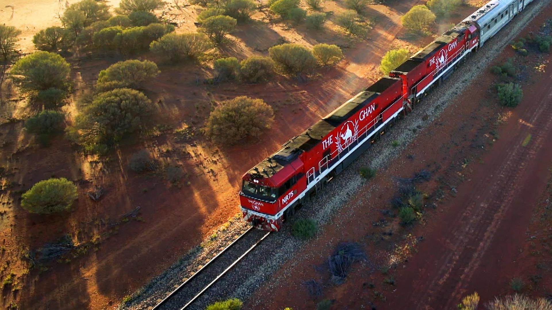 Luftbild: Ein langer Zug mit zwei Lokomotiven fährt durch eine weite Landschaft.