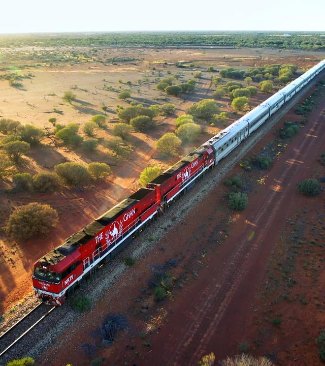 Luftbild: Ein langer Zug mit zwei Lokomotiven fährt durch eine weite Landschaft.