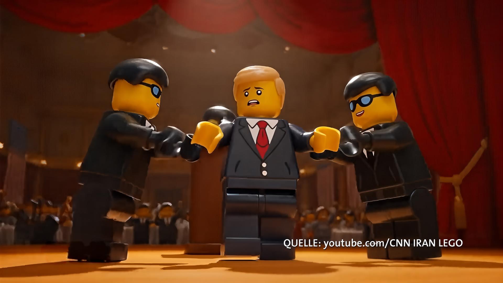 Zwei dunkelhaarige Lego-Männer in Anzügen halten einen blonden Lego-Mann mit Anzug und roter Kravatte von beiden Seiten fest.