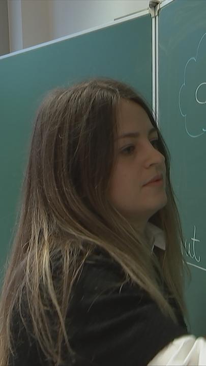 Auf dem Bild ist eine Ukrainische Lehrerin zu sehen, die an eine Tafel schreibt.