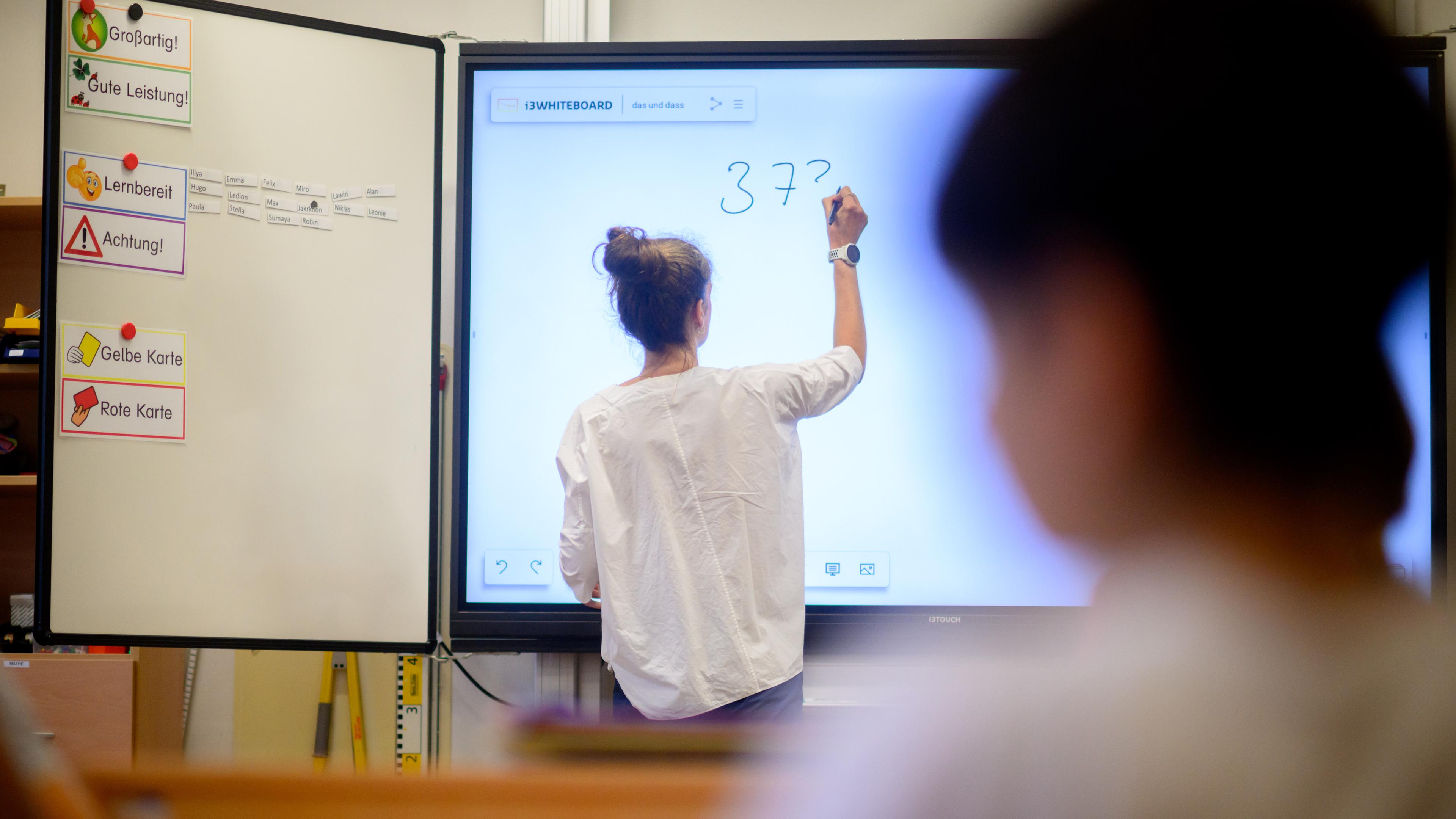  Eine Lehrerin schreibt eine Mathematikaufgabe auf eine digitale Schultafel im Klassenraum einer 4. Klasse einer Grundschule in der Region Hannover.