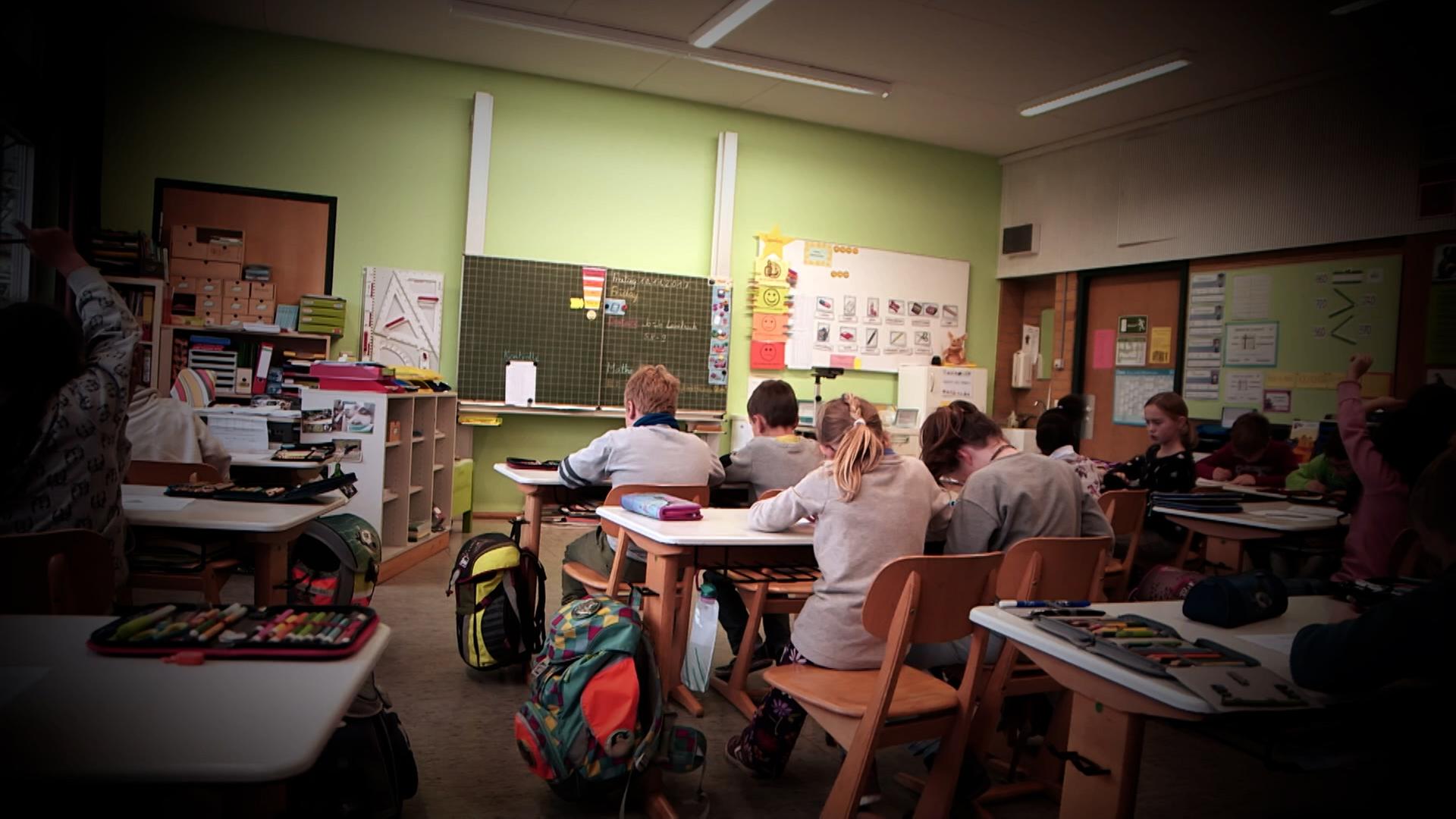 In einem Klassenzimmer sitzen Schülerinnen und Schüler an ihren Plätzen.