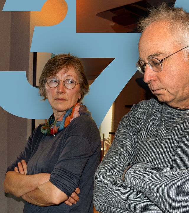 Eine Frau und ein Mann stehen nebeneinanderin der Wohnung und haben die Arme verschränkt.
