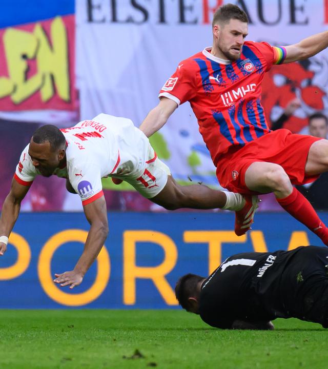 Leipzigs Lois Openda wird von Heidenheims Torhüter Kevin Müller und Patrick Mainka gestoppt.