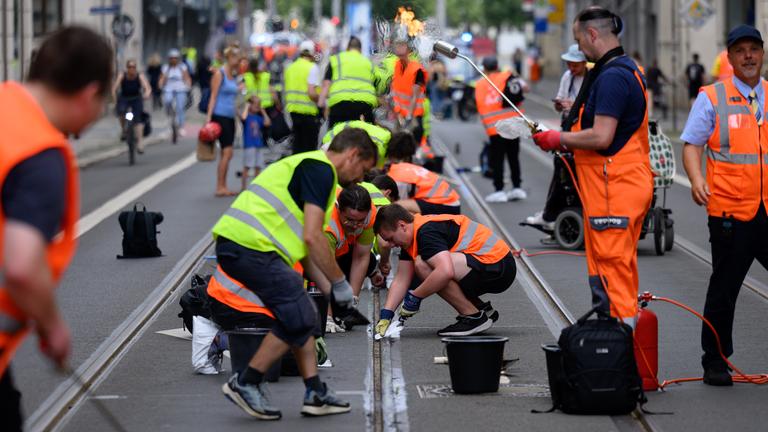 Freiwillige Helferinnen und Helfer befreien im Zentrum Straßenbahnschienen von verklebter Fugenmasse. 