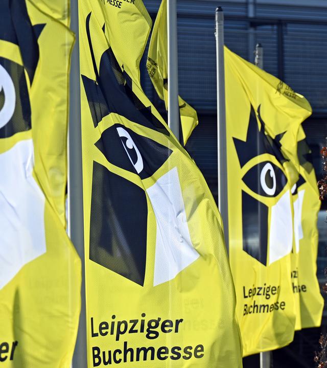 Gelbe Fahnen mit einem stilisierten schwarzen Auge über einem Buch  flattern im Wind.