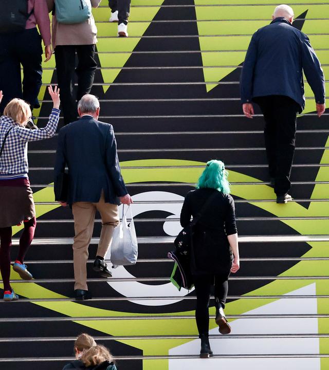 Menschen laufen über eine Treppe mit Logo der Leipziger Buchmesse 2026