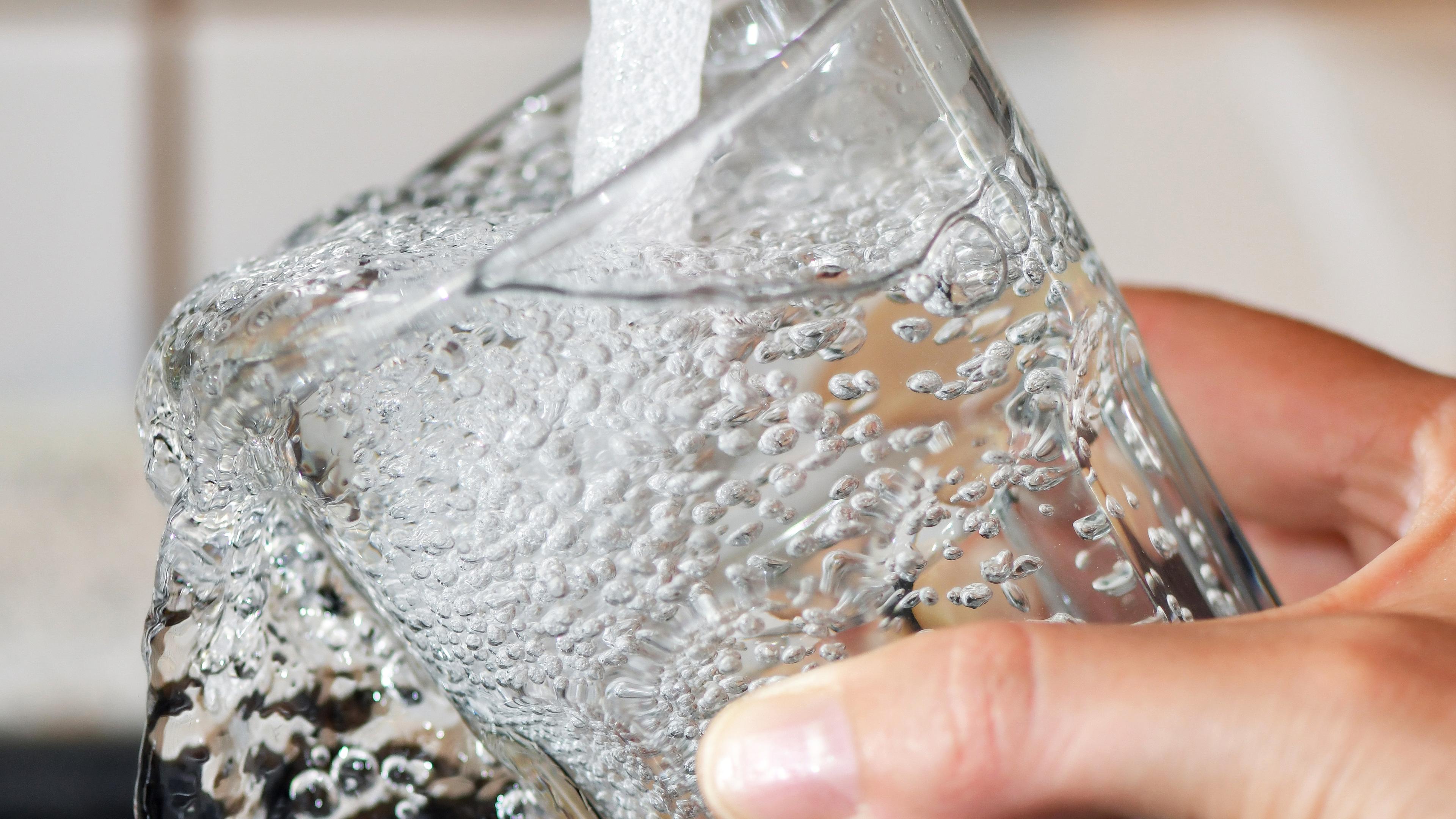 Ein Trinkglas wird an einem Wasserhahn mit Leitungswasser befüllt. 