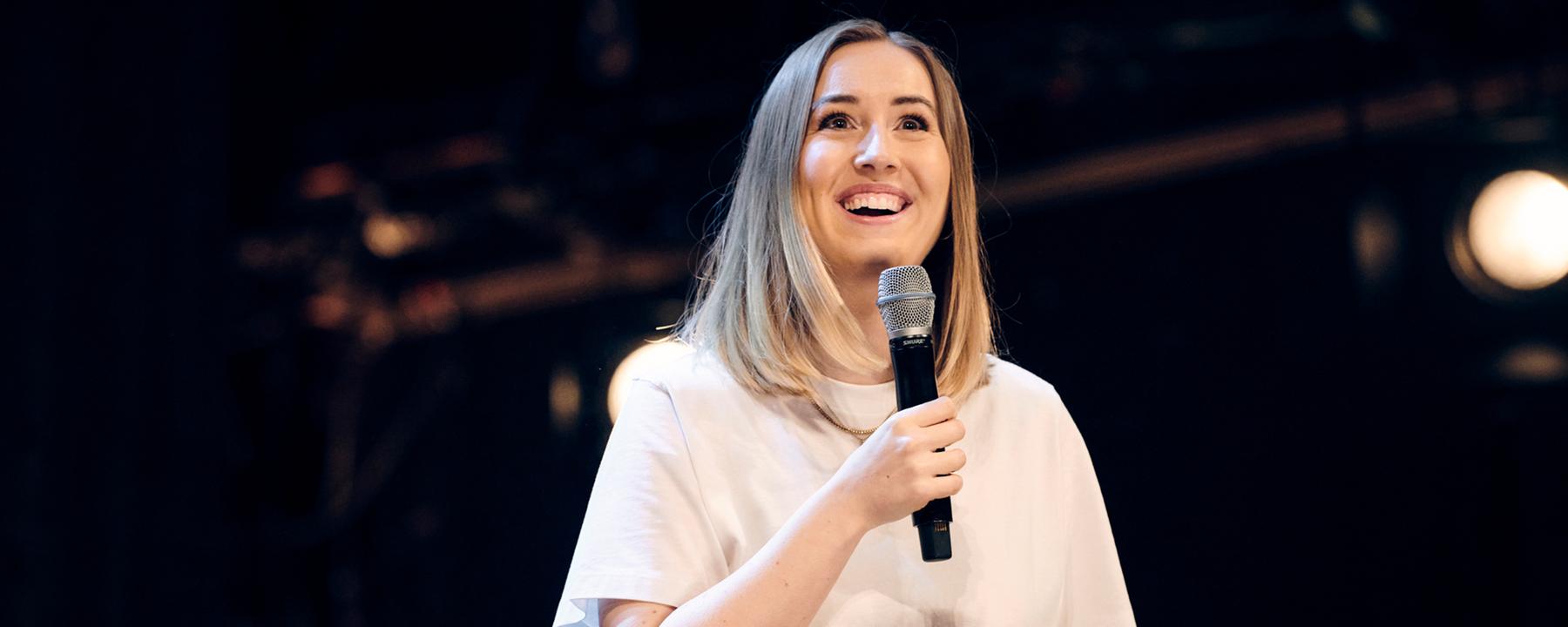 Lena Kupke steht auf einer dunklen Bühne. 