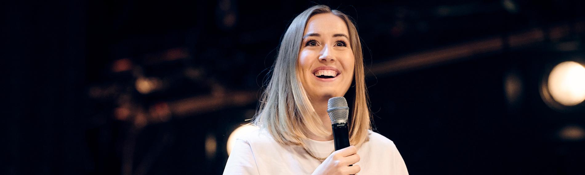 Lena Kupke steht auf einer dunklen Bühne. 