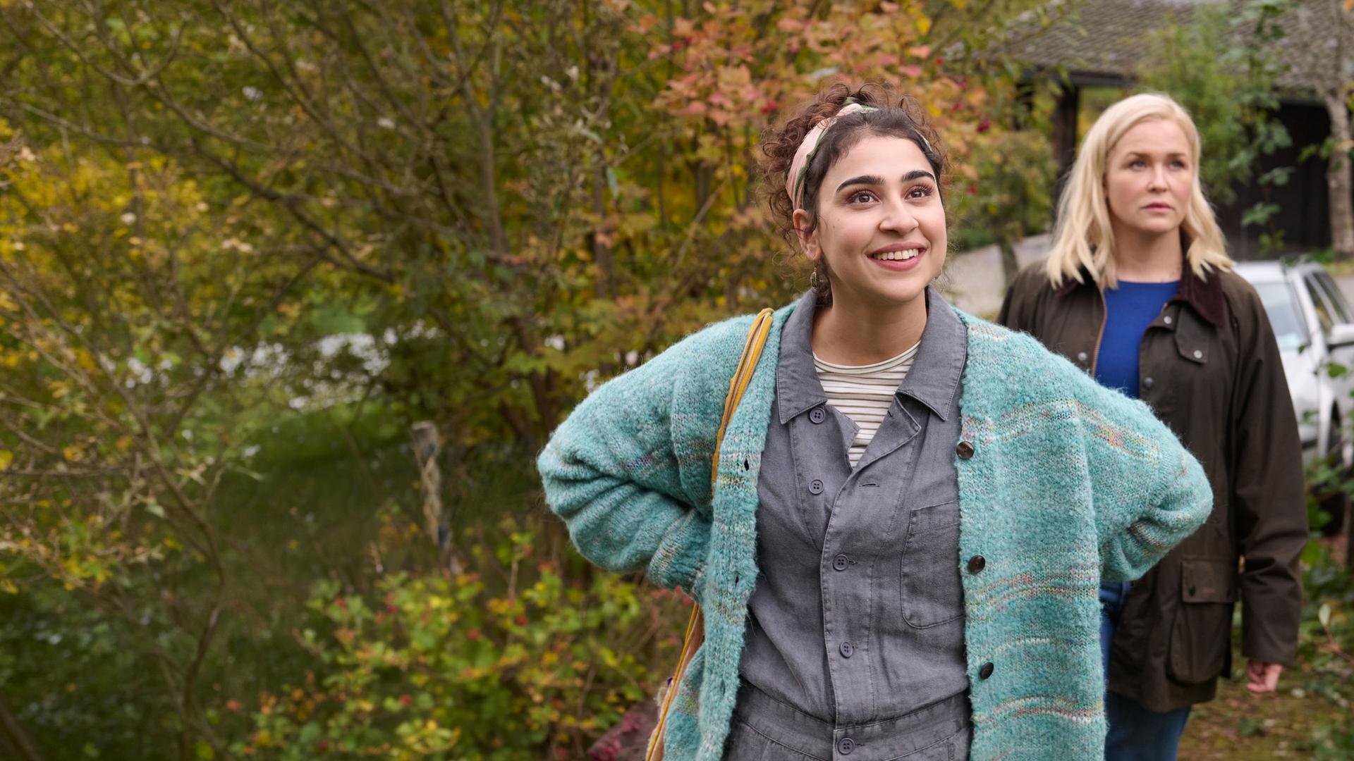 "Lena Lorenz - Benita und Muck": In einem Vorgarten stehen Benita Schickler (Hannah Gharib) und Lena Lorenz (Judith Hoersch). Benita hat die Hände in die Hüfte gestützt und blickt strahlend nach oben, während Lena Lorenz (Judith Hoersch) mit skeptischem Blick in die gleiche Richtung schaut.