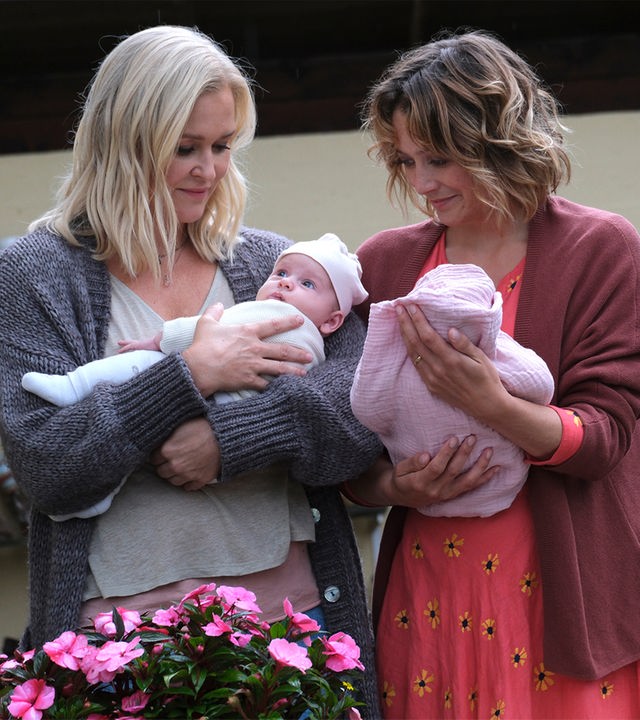 "Lena Lorenz - Das halbe Lottchen": Auf einer Terrasse stehen Lena Lorenz (Judith Hoersch) und Magali Bernbauer (Hanna Plaß) nebeneinander. Jede hält eines der beiden Zwillingsmädchen im Arm.