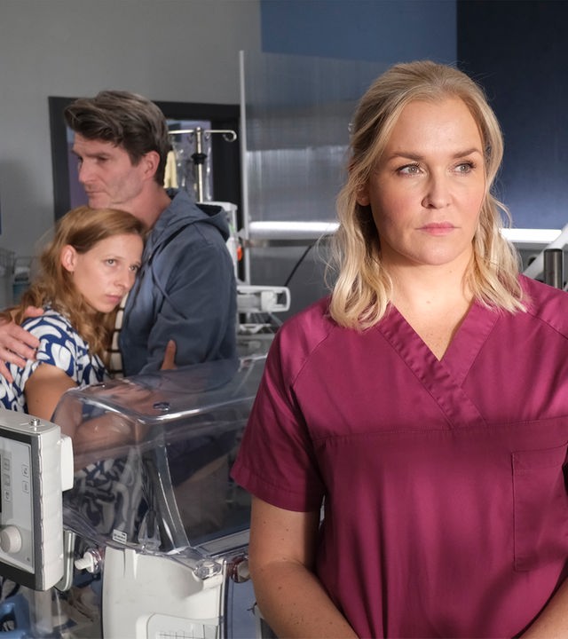 "Lena Lorenz - Gefährliche Liebe": Im Intensivzimmer einer Kinderstation steht Lena Lorenz (Judith Hoersch) und schaut besorgt in die Ferne. Hinter ihr stehen Jasmin Pohl (Mattea Cavic) und Moritz Greinert (Leopold Hornung), die sich mit traurigem Gesichtsausdruck in den Armen halten.