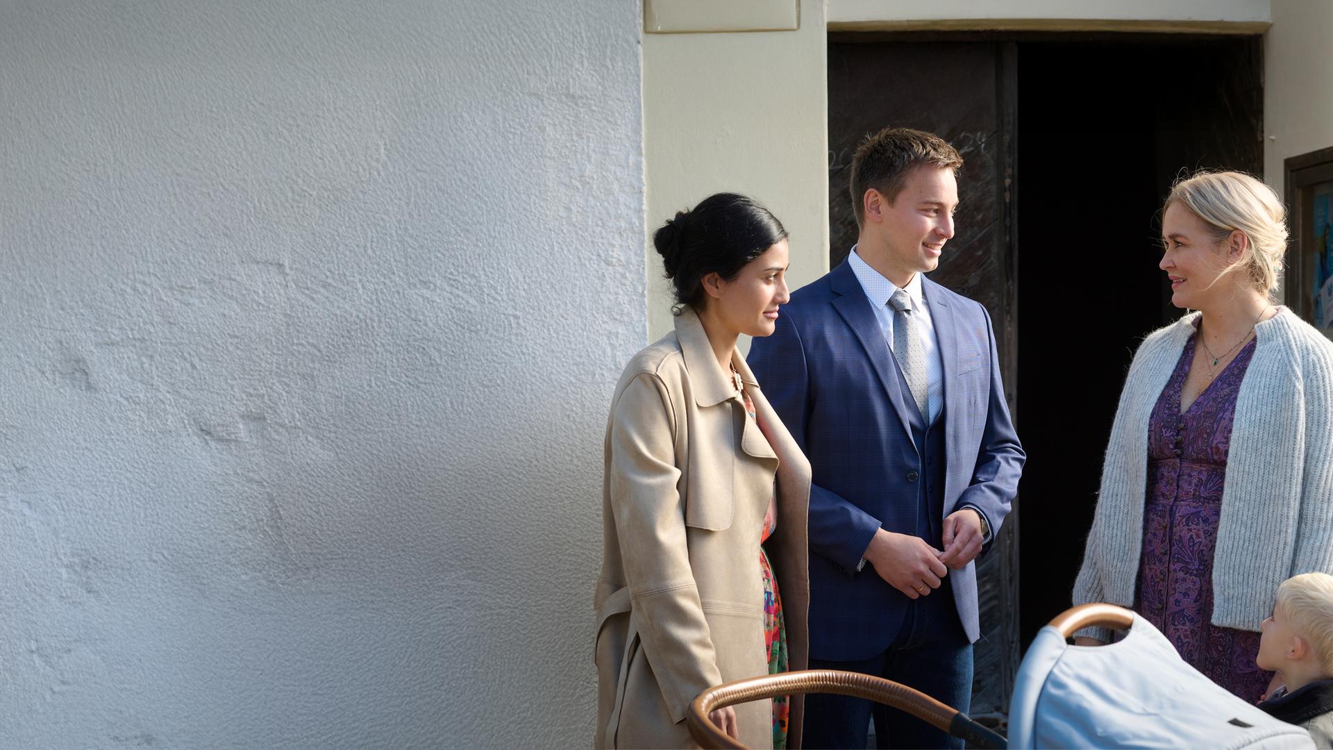 "Lena Lorenz - Überväter": Vor einer Kirchentür stehen Greta (Sogol Faghani) und Ferdinand Junghans (Timmi Trinks) mit einem Kinderwagen und unterhalten sich mit Lena Lorenz (Judith Hoersch), die ihren kleinen Sohn Luis (Samuel Gerbrich) an der Hand hält.