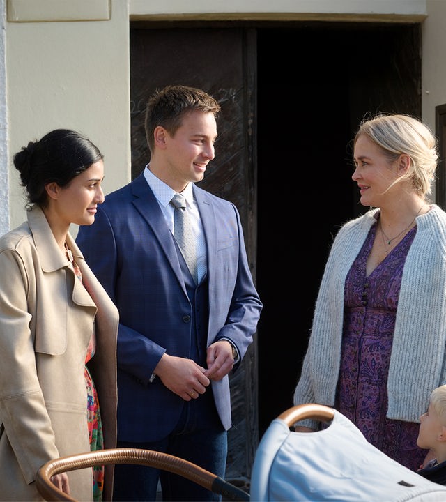 "Lena Lorenz - Überväter": Vor einer Kirchentür stehen Greta (Sogol Faghani) und Ferdinand Junghans (Timmi Trinks) mit einem Kinderwagen und unterhalten sich mit Lena Lorenz (Judith Hoersch), die ihren kleinen Sohn Luis (Samuel Gerbrich) an der Hand hält.