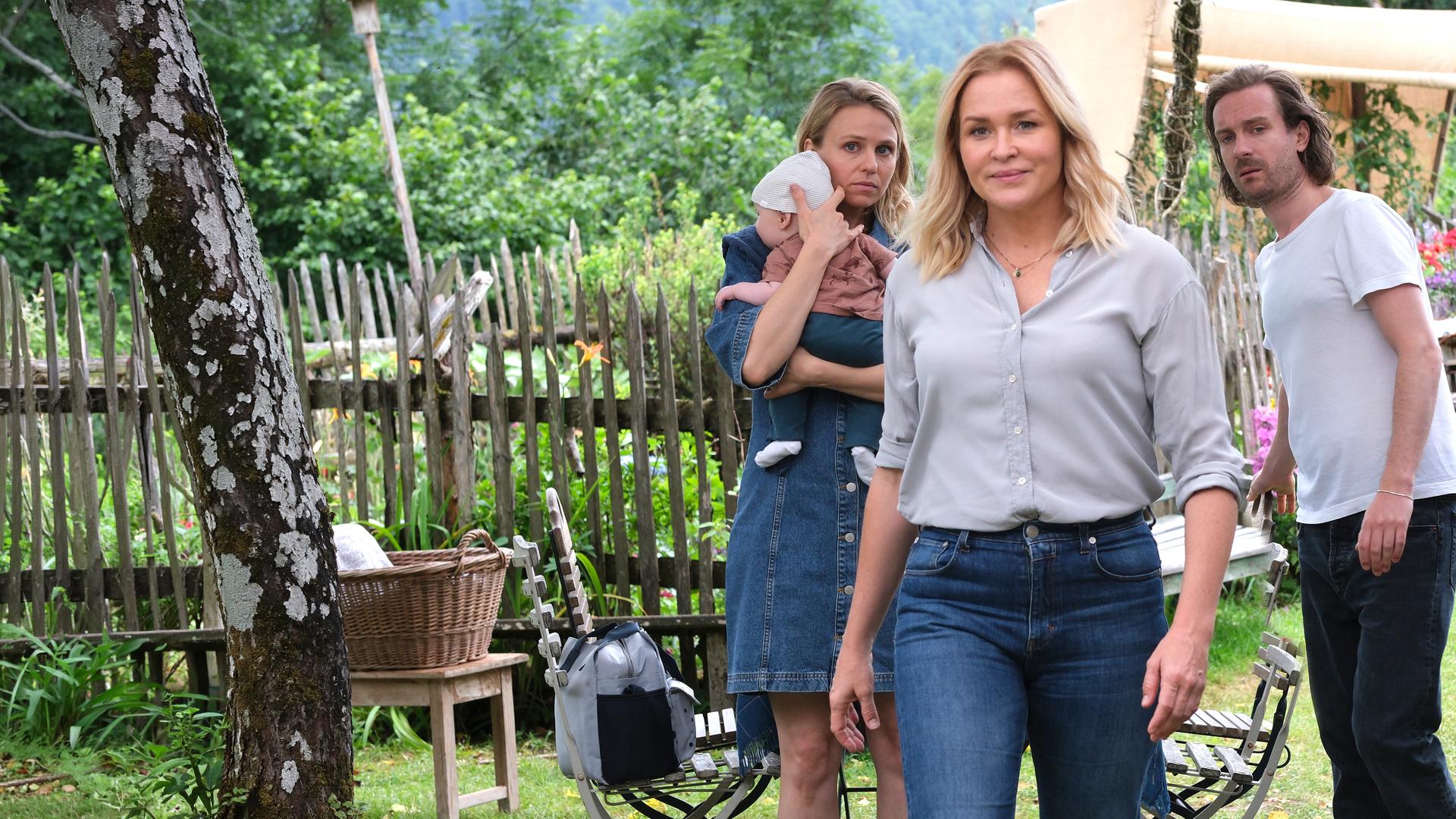 "Lena Lorenz - Vertauscht": Im Garten des Lorenzhofes sitzen Gregor (Nicholas Reinke) und Mareike Völler (Anja Antonowicz),  Lena Lorenz (Judith Hoersch) und Raffael Vollmer (Max Rothbart). Alle schauen Annika (Teresa Rizos) hinterher, die ihr Baby an sich drückt und mit besorgtem Gesichtsausdruck den Tisch verlässt.