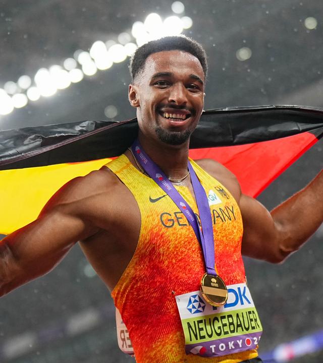 Leo Neugebauer ist Zehnkampf-Weltmeister. Er posiert mit einer Deutschlandflagge und schaut lächelnd in die Kamera.